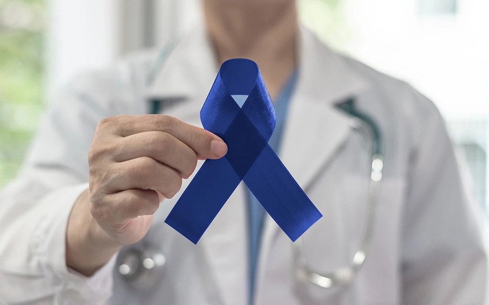 A colorectal cancer specialist holding a blue ribbon in support of colorectal cancer